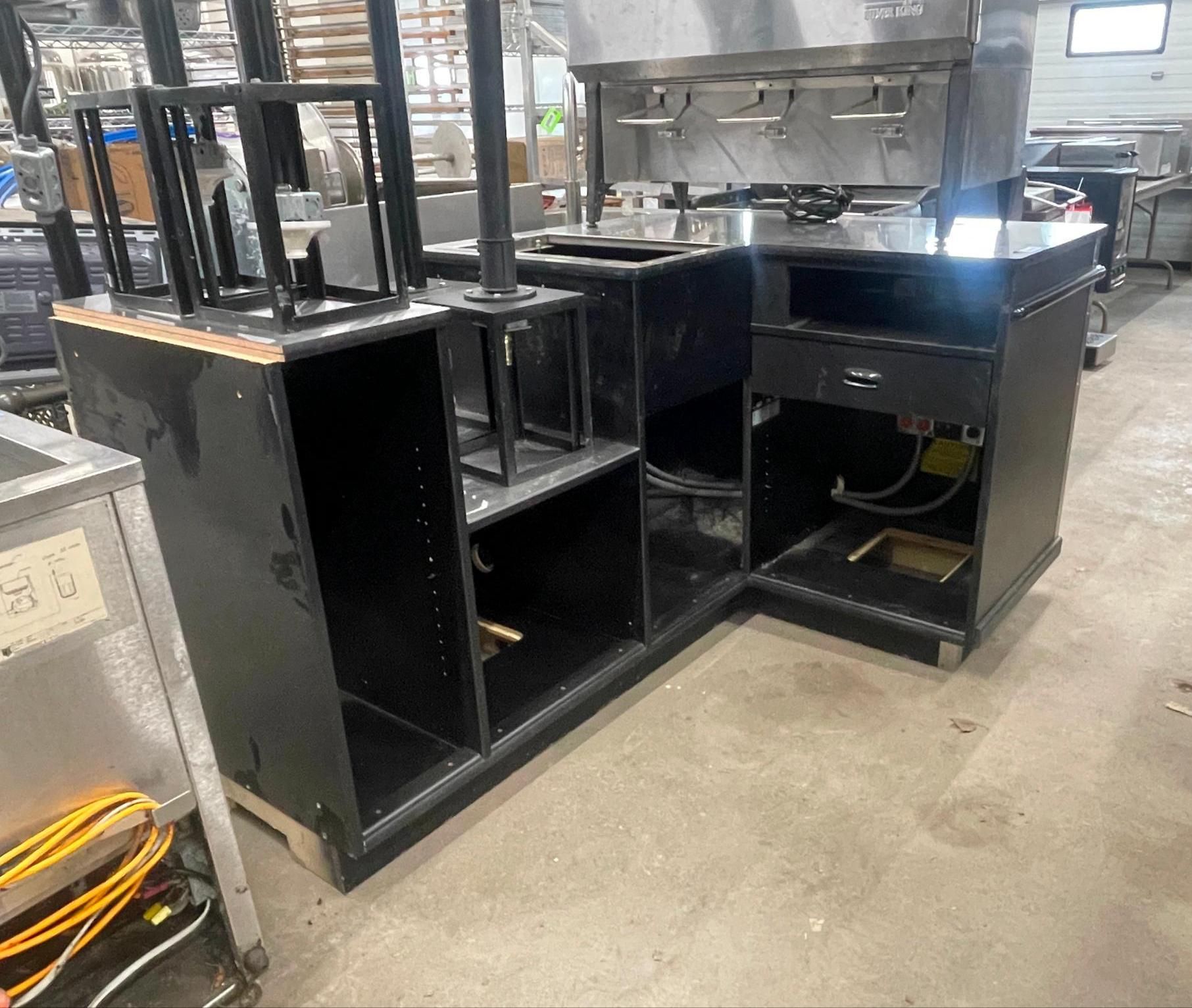 Black metal workstations in an industrial kitchen or workshop with shelves and equipment.
