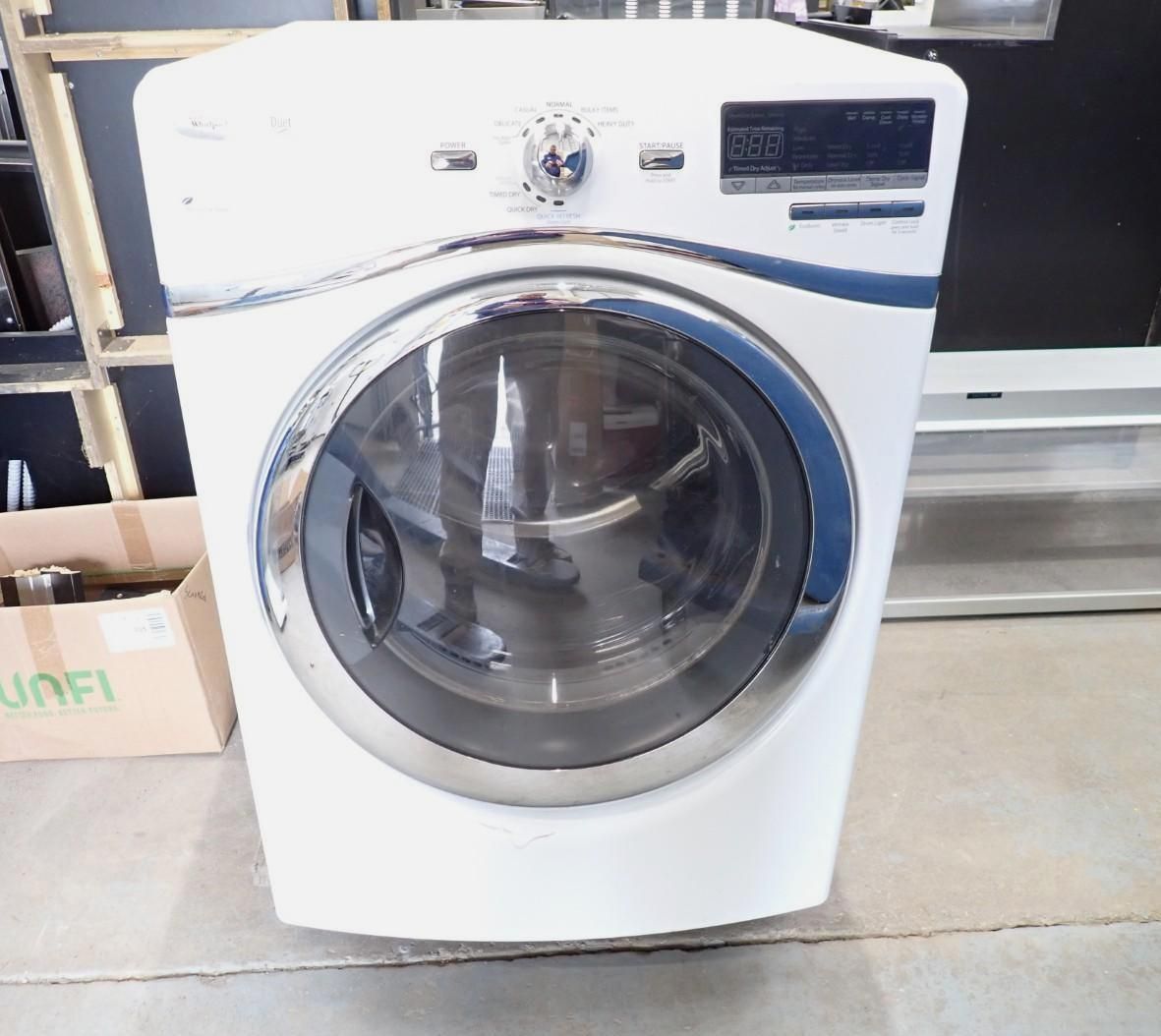White front-loading washing machine with a round glass door in a laundry or storage area