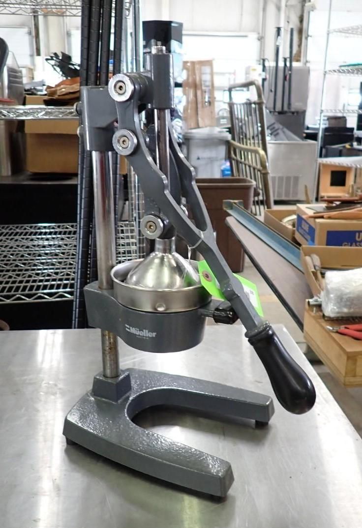 Manual citrus juicer on stainless steel counter in a kitchen or restaurant prep area