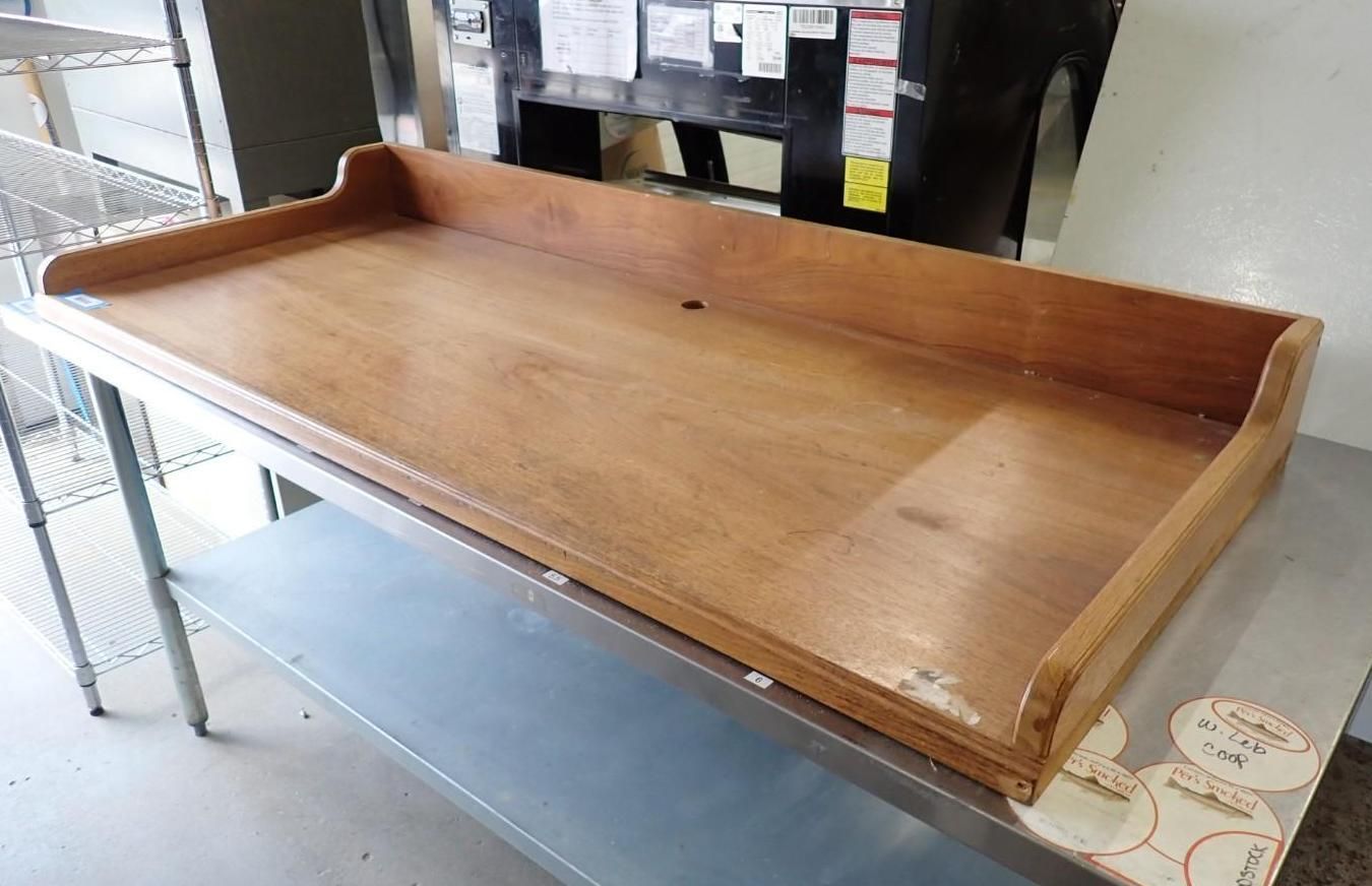 Wooden serving tray with raised sides on a metal table in a workshop area