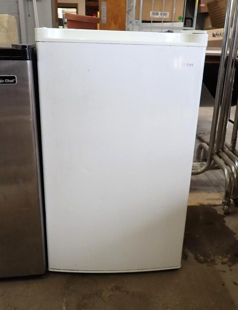White chest freezer in a garage, standing beside a stainless steel appliance.