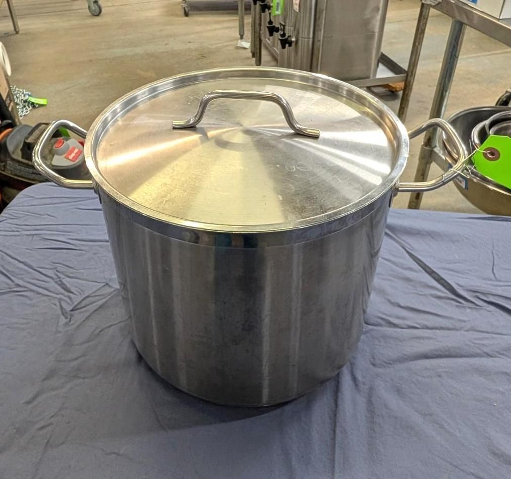 Large stainless steel stock pot with lid on a table in a kitchen or catering area