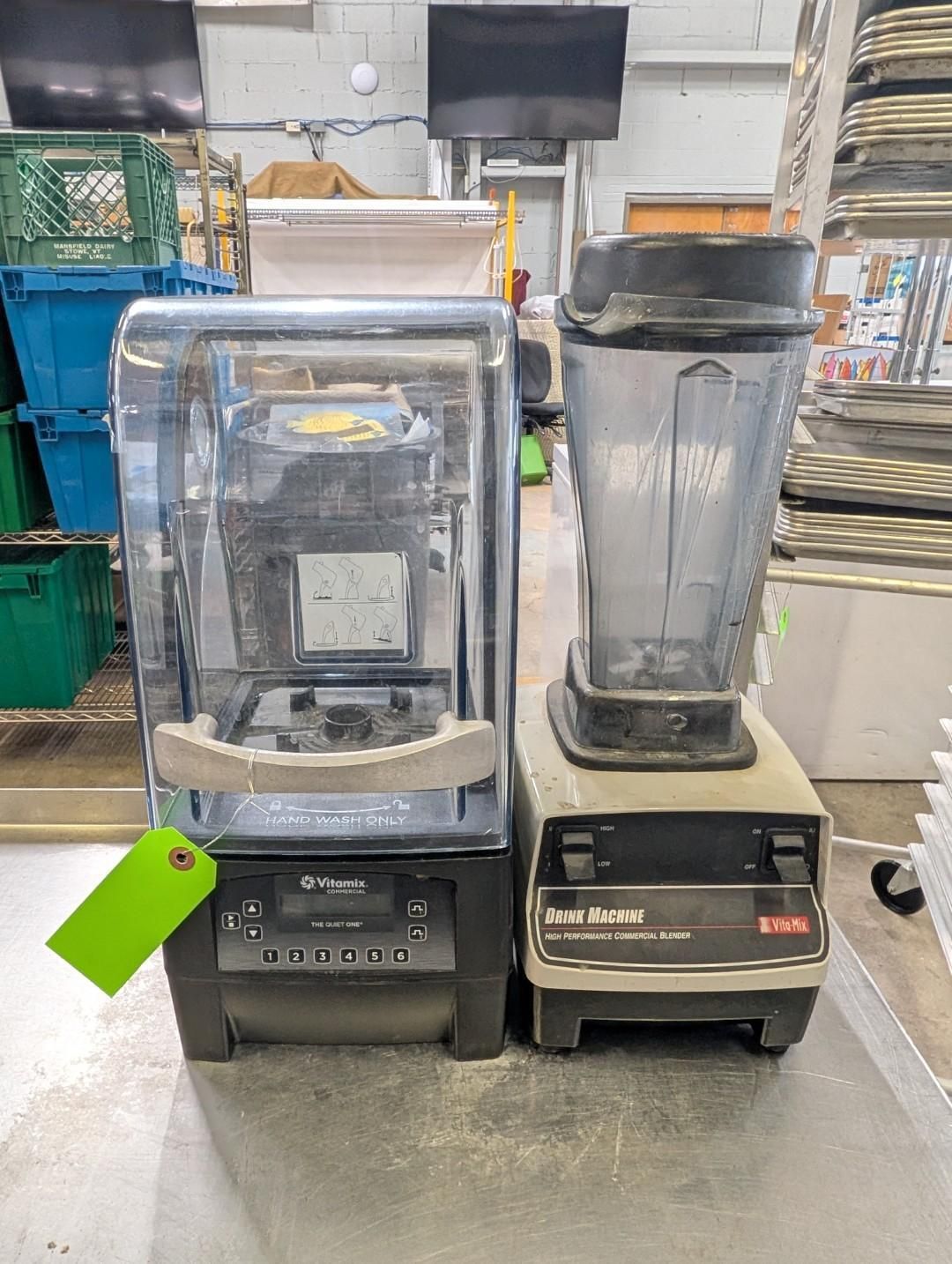 Two blenders on a counter in a kitchen or food prep area, one with a cover and one empty.