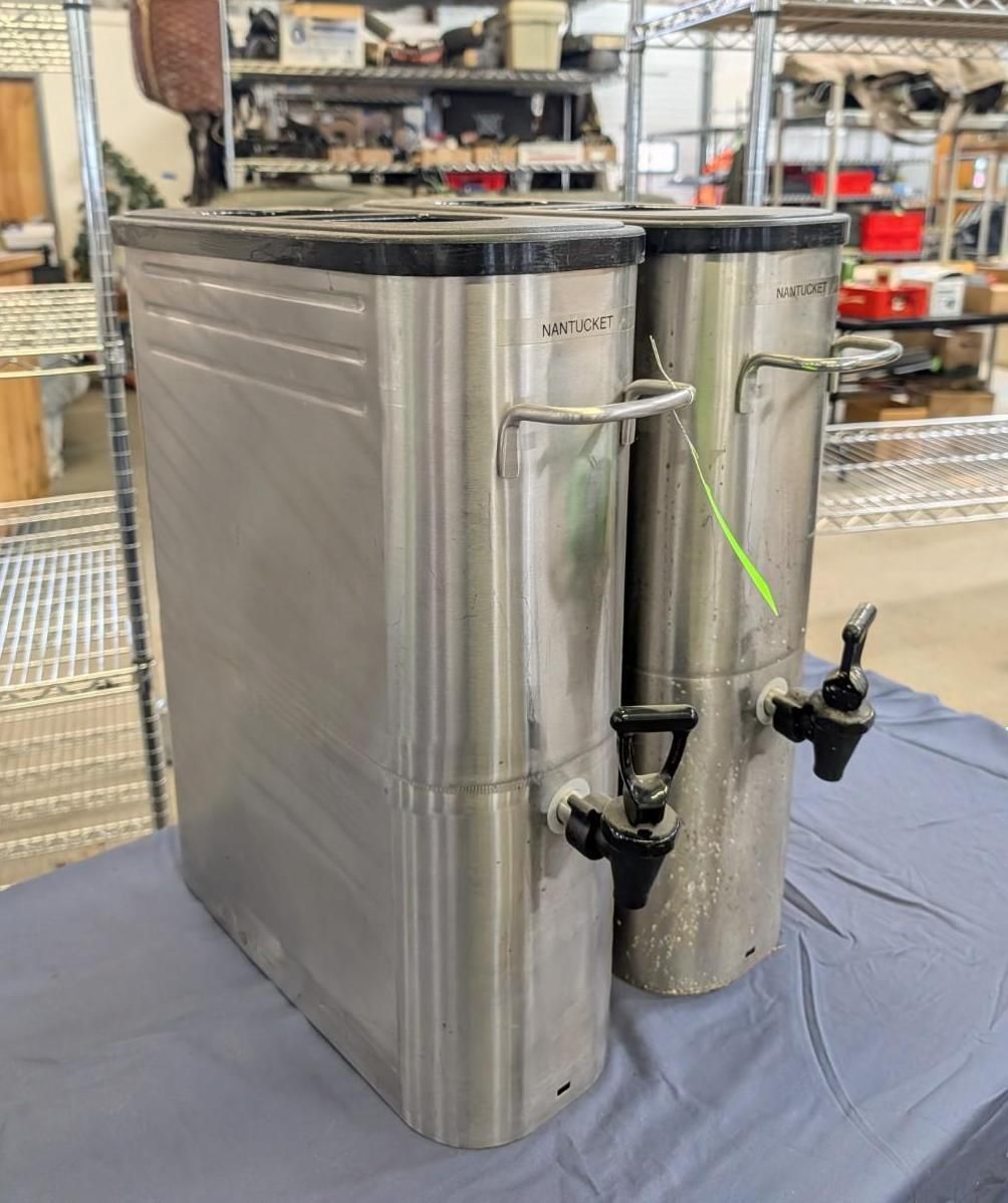 Stainless steel water tank with attached cylinder and faucet, displayed on a table in a workshop.