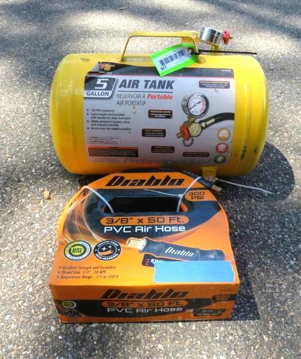 Yellow air tank and coiled black air hose in a cardboard box. Both sit on asphalt.