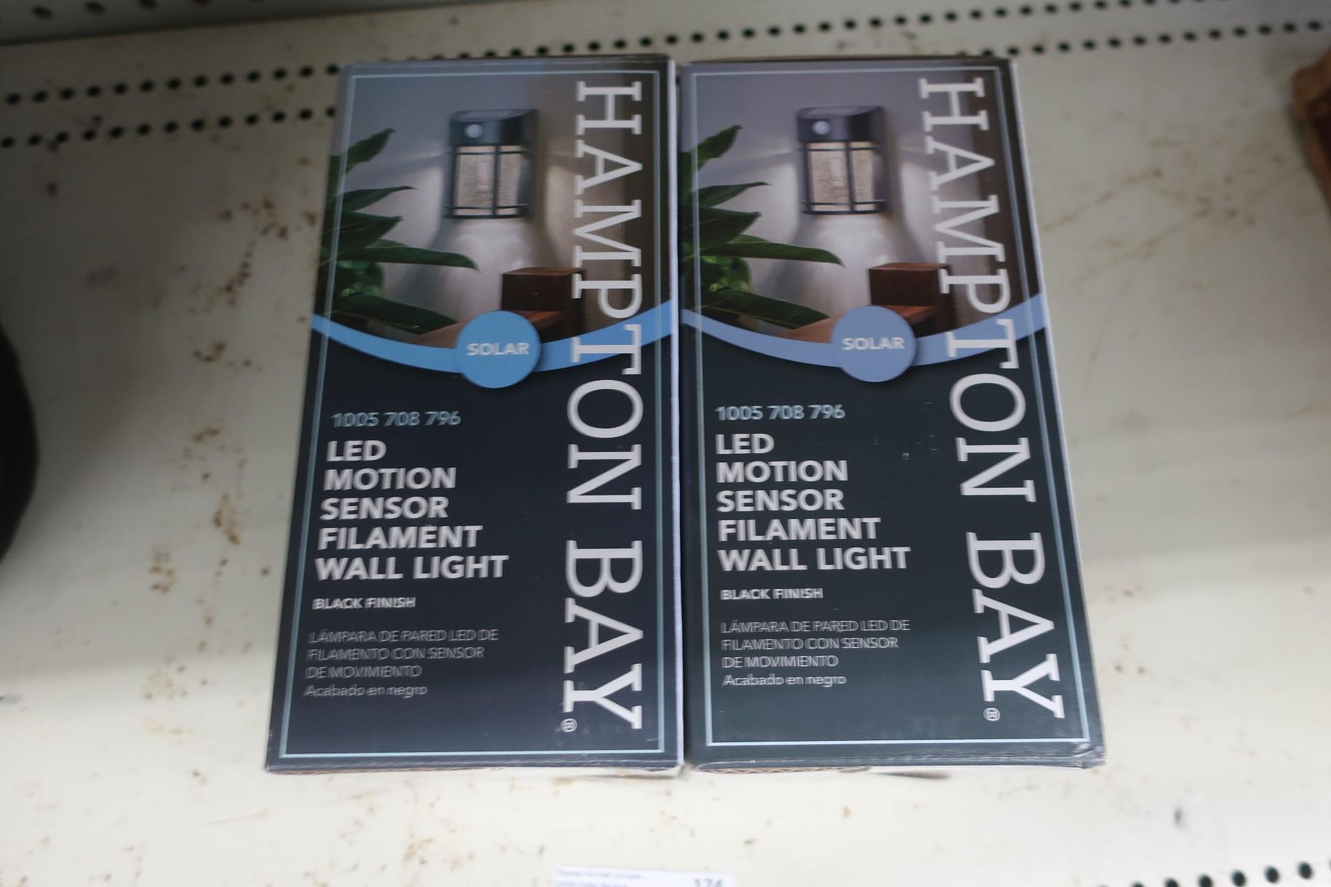 Two Hampton Bay LED motion sensor filament wall light boxes on a shelf.