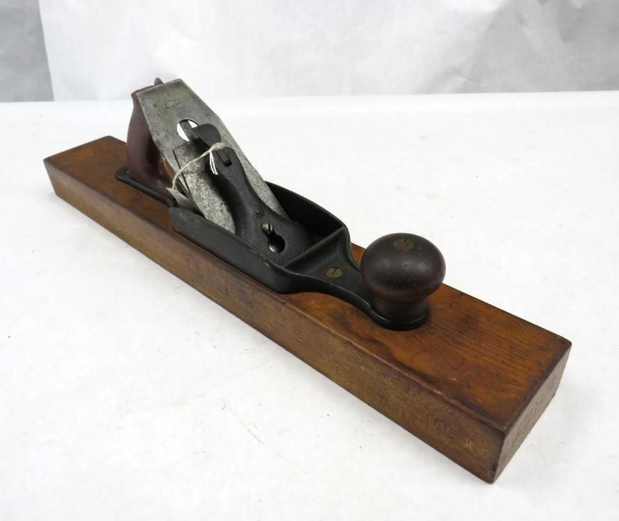 A wooden hand plane, dark metal blade and handle on a brown base.