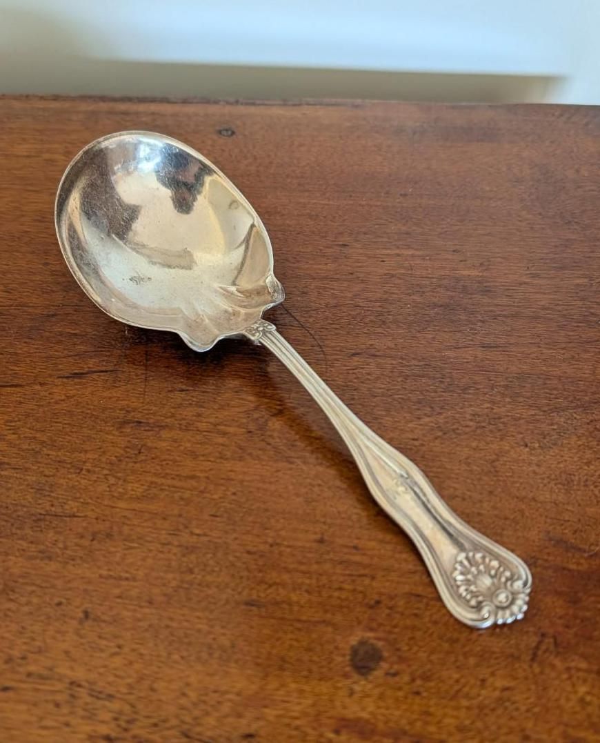 A silver-colored spoon with an ornate floral handle design resting on a polished wooden surface.