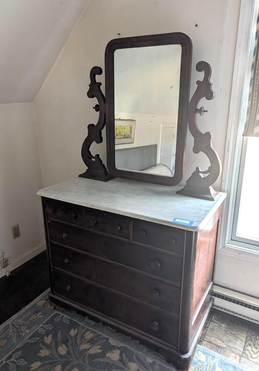 A dark wood Victorian-style dresser with a marble top and a large, ornate mirror with scrollwork side supports.