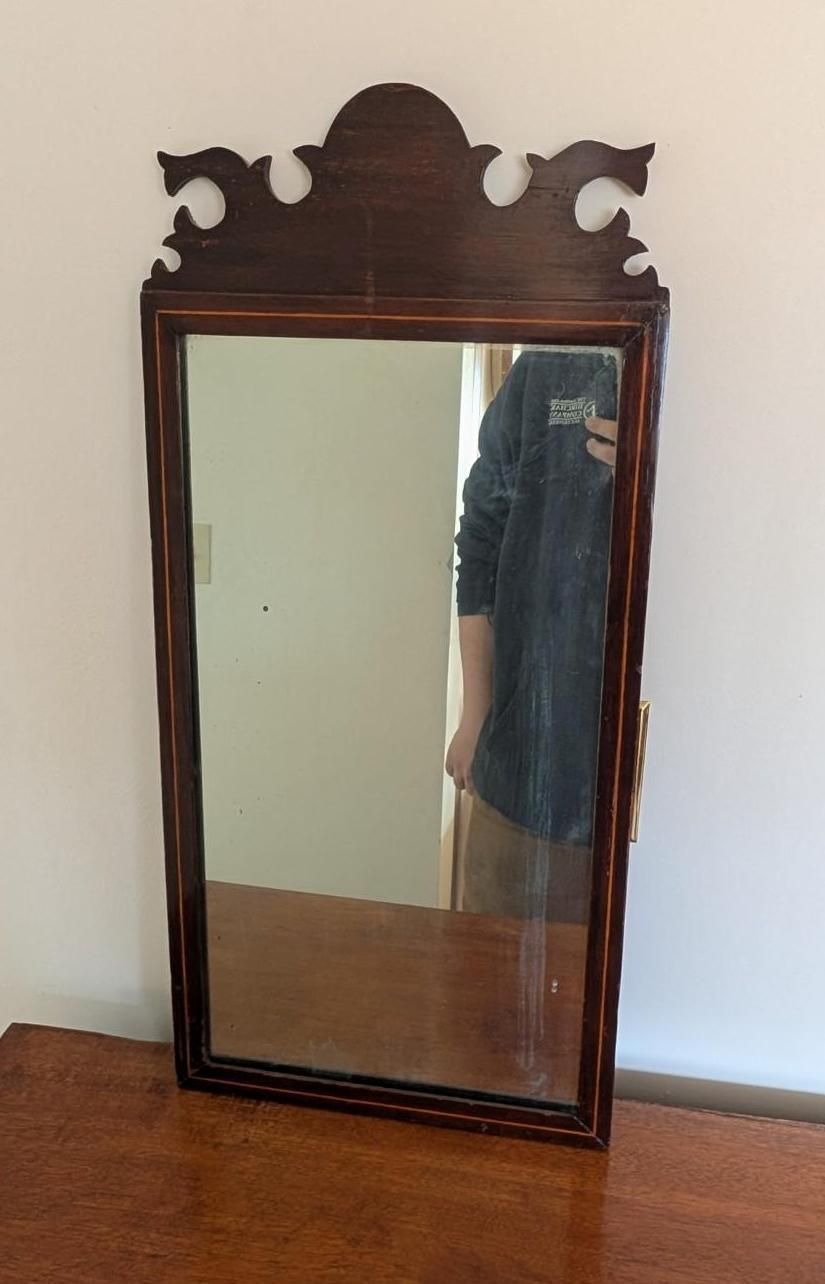 A rectangular wooden wall mirror with a decorative scrolled crest and dark finish.