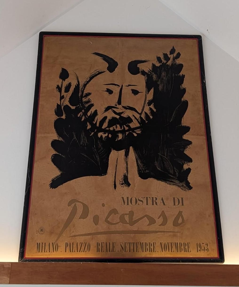 A poster for a 1953 Picasso exhibition in Milan featuring a black ink drawing of a faun on a tan background.