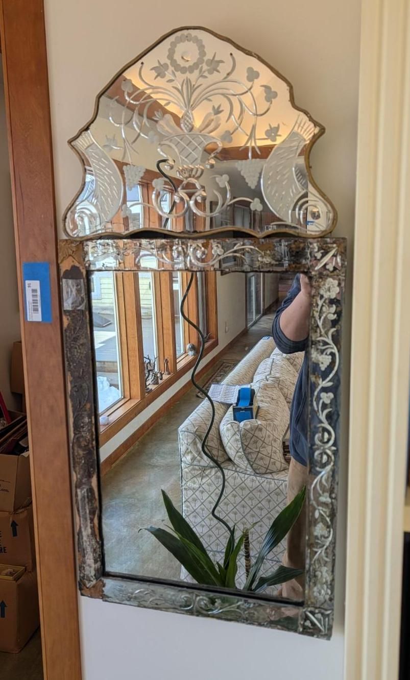 An ornate, rectangular wall mirror with a decorative, arched crest featuring etched floral patterns and aged glass.