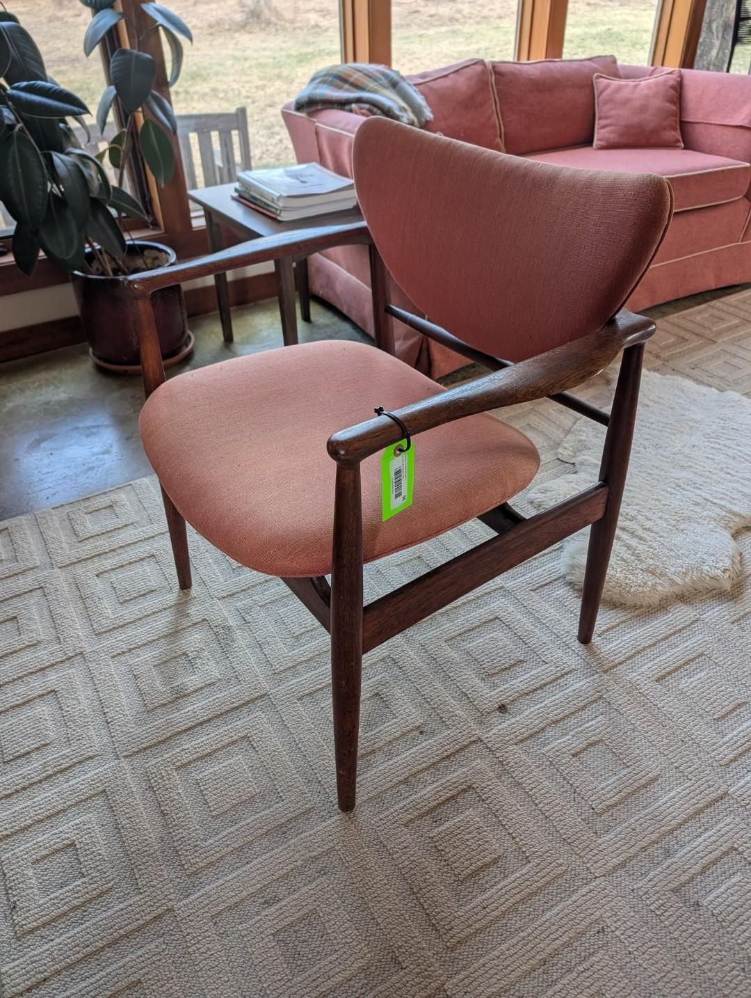 A mid-century modern wooden armchair with coral-colored fabric upholstery, placed on a rug in a living room.