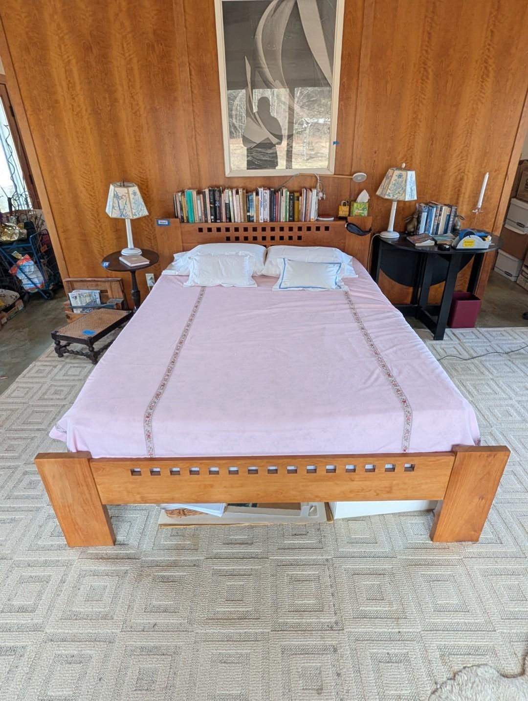 A bedroom features a wooden bed with a pink spread, flanked by small tables with lamps, set against wood-paneled walls.