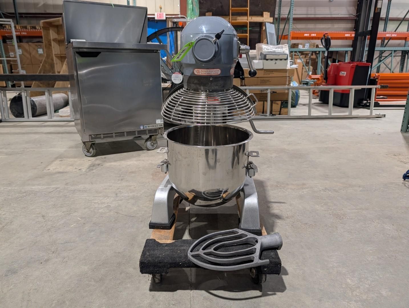 Industrial mixer in a workshop, with a metal bowl and coiled hose on the base.