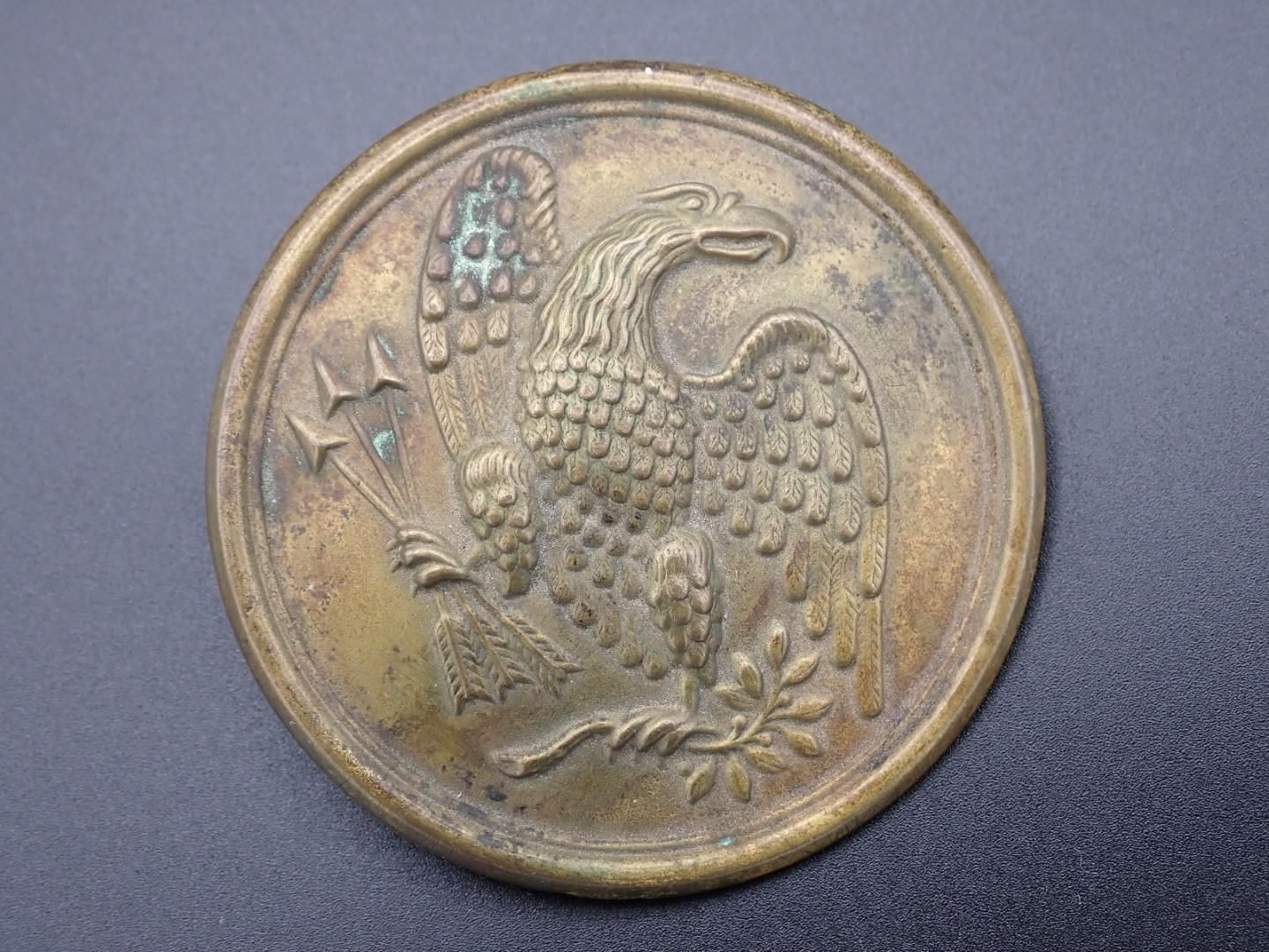 A round brass button with an eagle clutching arrows and a laurel branch.