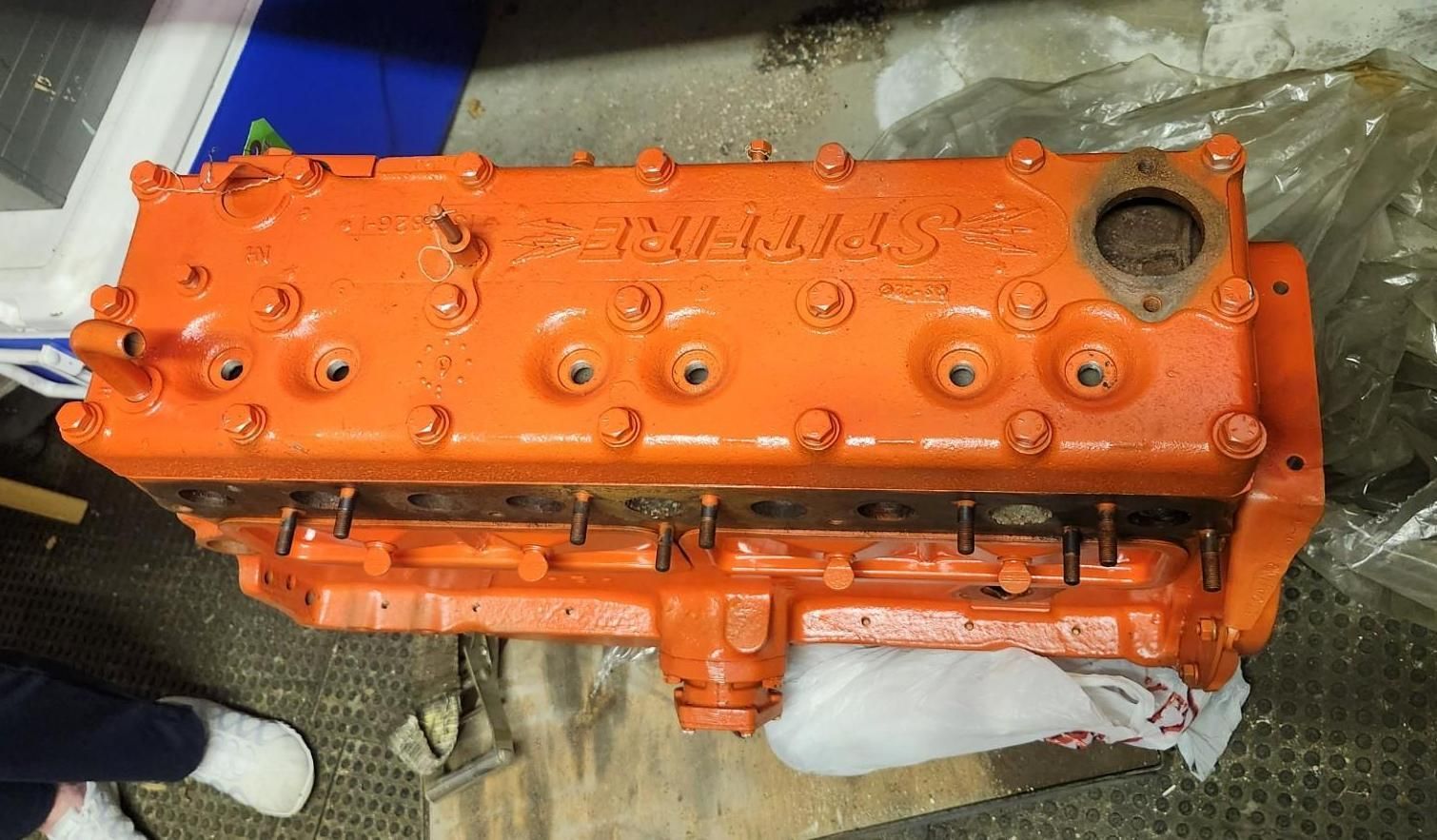 Orange engine block on a workbench, viewed from above, with hoses and tools around it.
