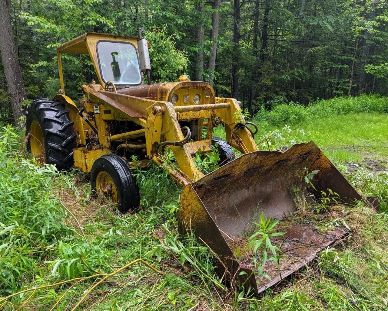 yellow backhoe with front bucket in a wooded area