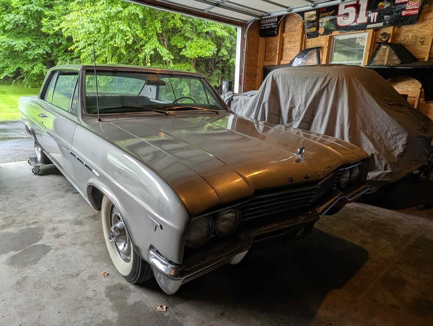 Vintage gray car parked in a garage beside a covered vehicle