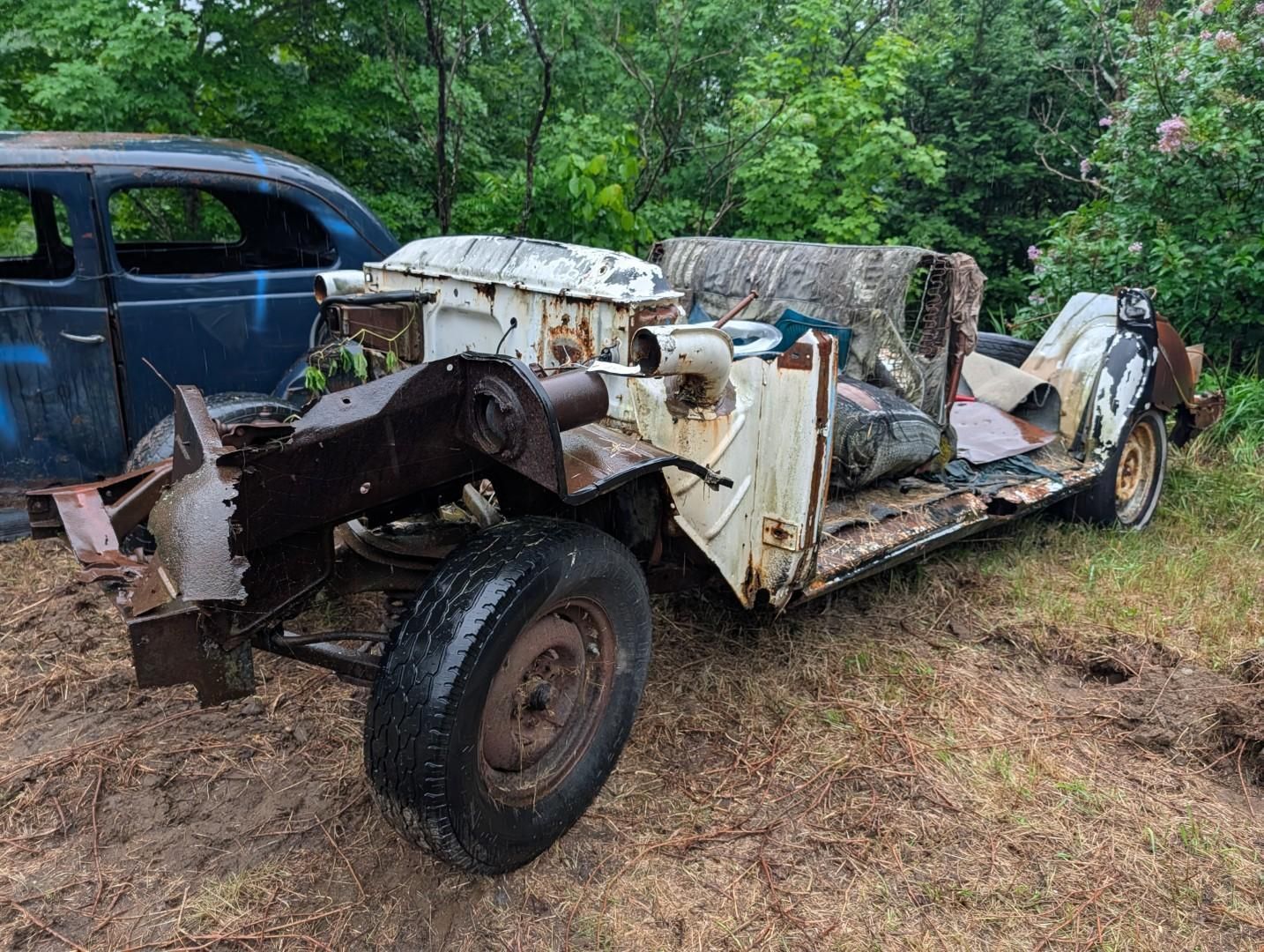 antique car frame in a wooded yard