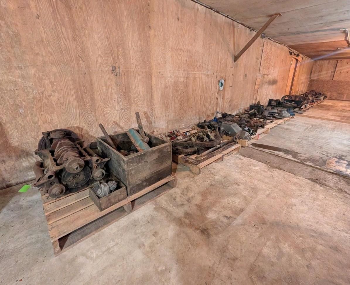 Long row of dark bundles and crates stored along a rough concrete wall in a bare room.