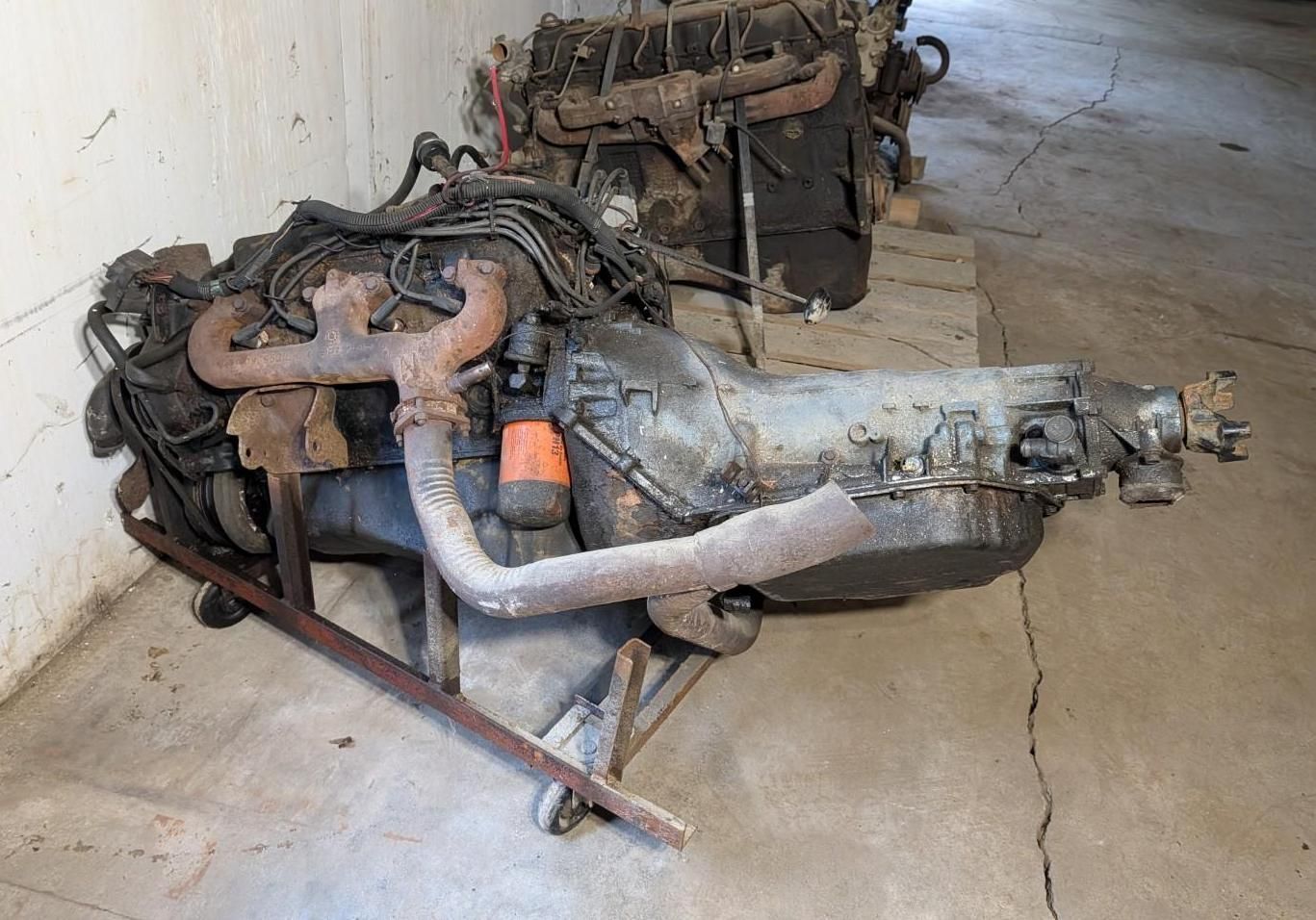 Detached car engine and transmission assembly on a concrete floor in a garage.
