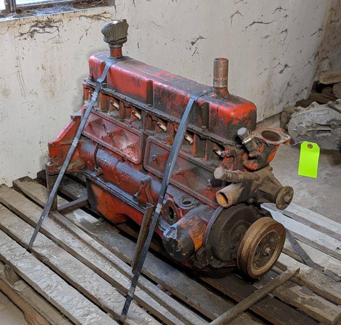 red engine block strapped to a wooden pallet in a garage or workshop.