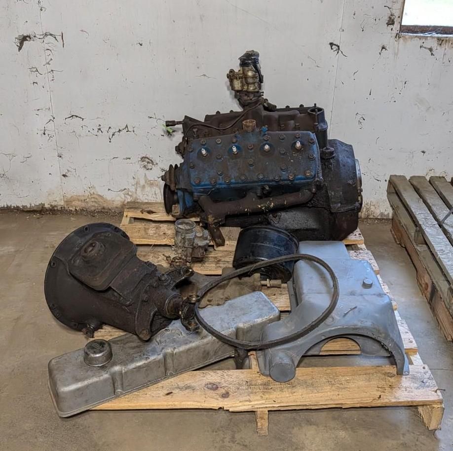 engine parts and a black mask-like object arranged on a wooden pallet against a wall.