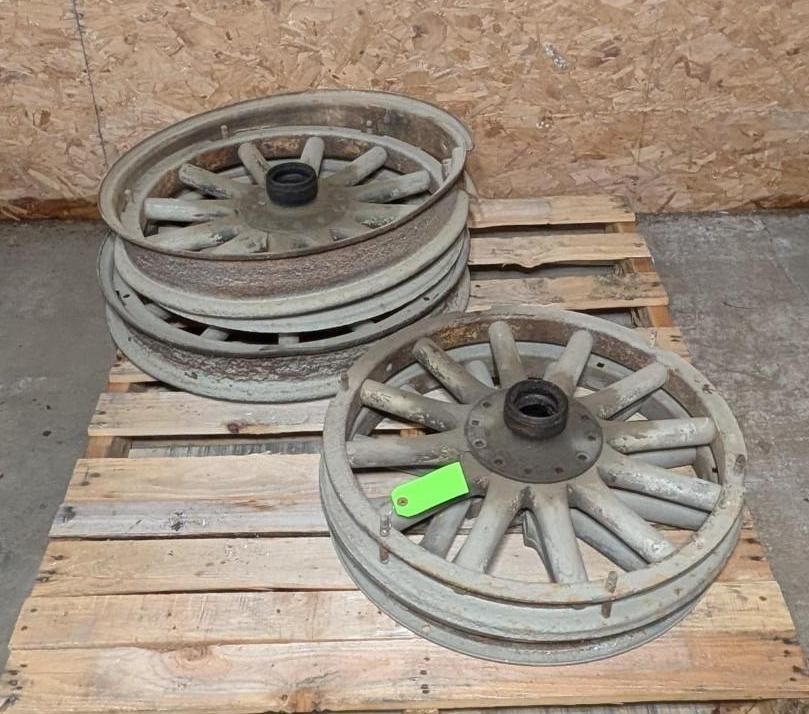Stacked metal wagon wheels on wooden pallets in a warehouse setting.