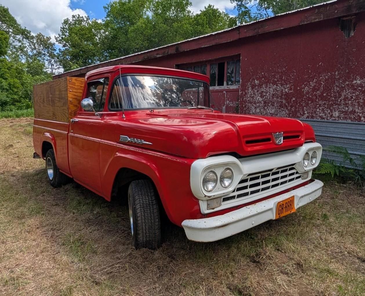 Red vintage pickup truck parked beside a red building on a grassy lot.