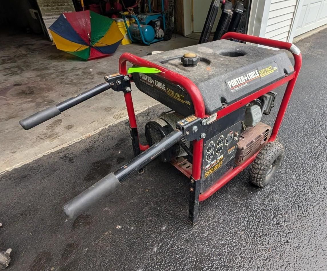 Red and black portable generator with two long black pipes, sitting on a driveway in a garage setting
