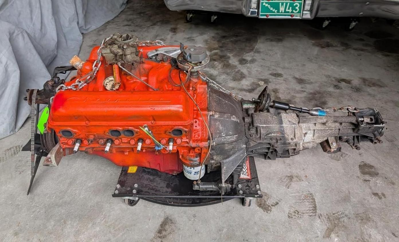 Bright orange car engine and transmission on a garage floor beside a vehicle underside