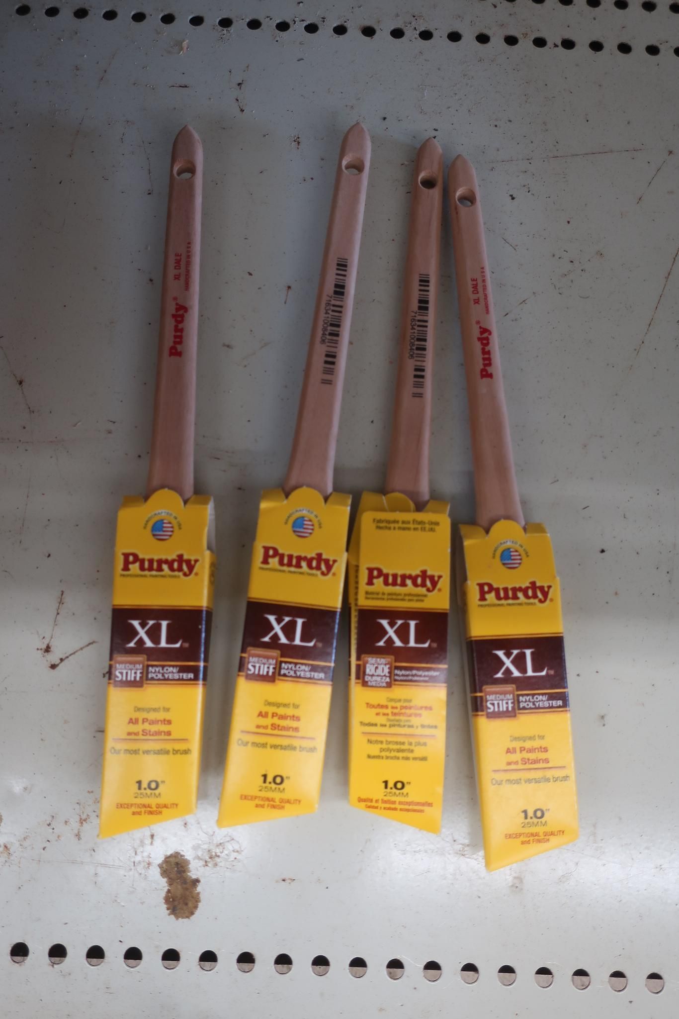 Four Purdy XL paint brushes with yellow and brown labels, arranged on a surface.