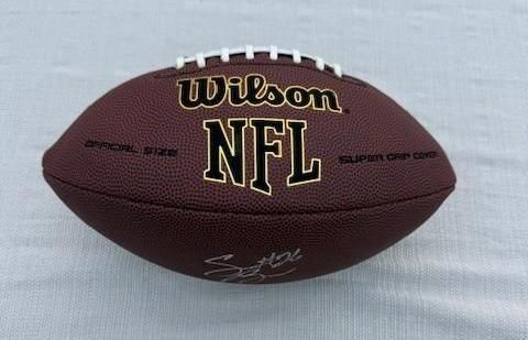 Football, brown Wilson NFL ball with white laces, resting on a white surface. Autographed.