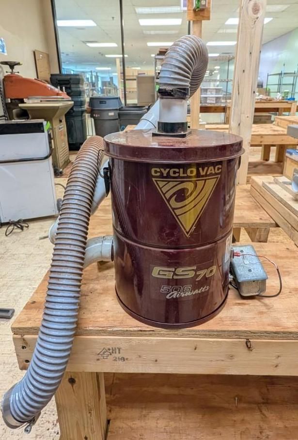 Maroon Cyclo Vac vacuum on a wooden workbench in a workshop, with hose and power cord attached
