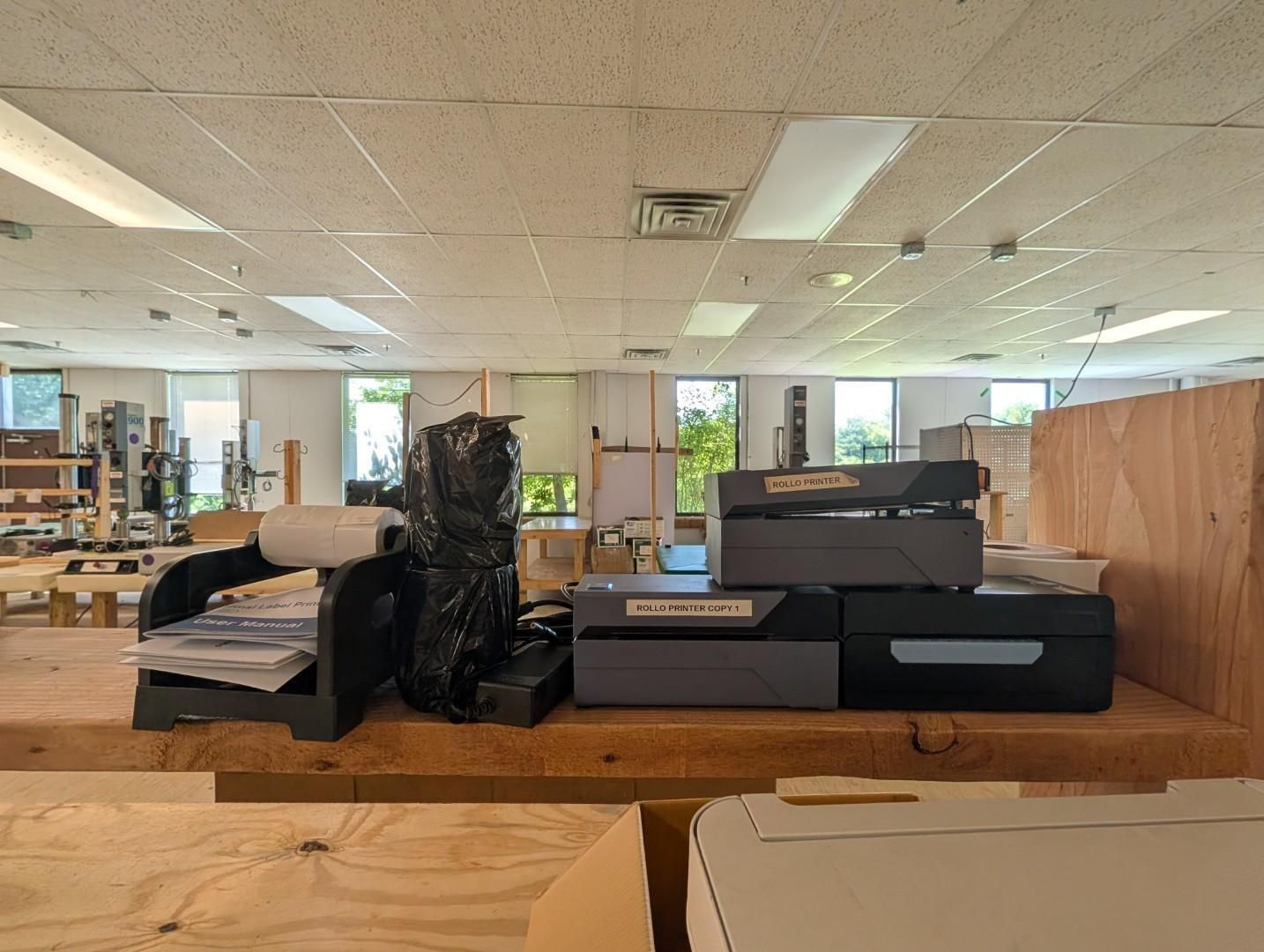 Office interior with desks, stacked papers, boxes, and plants under fluorescent ceiling lights