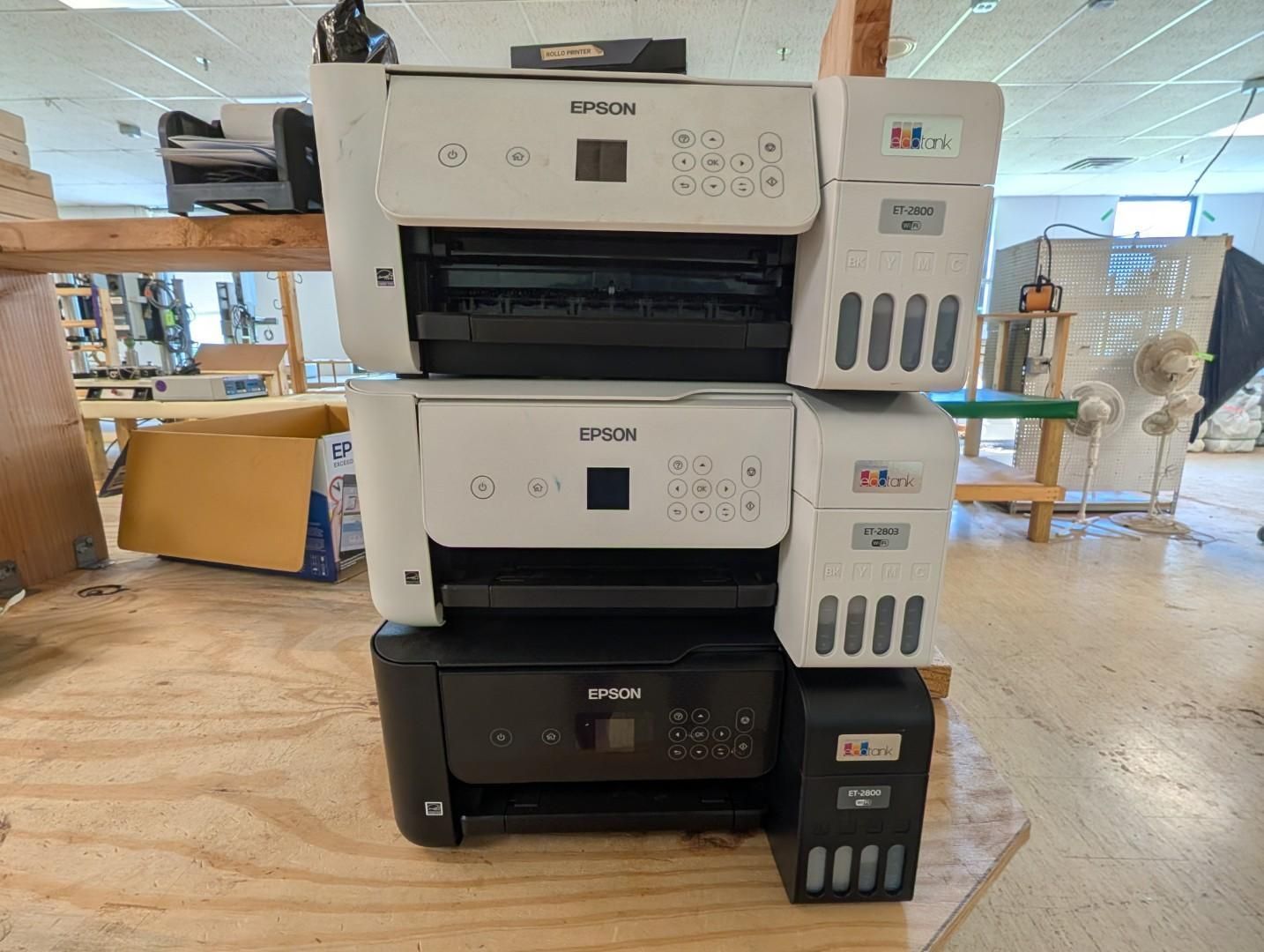 Three Epson printers stacked on a table in a workshop or store setting