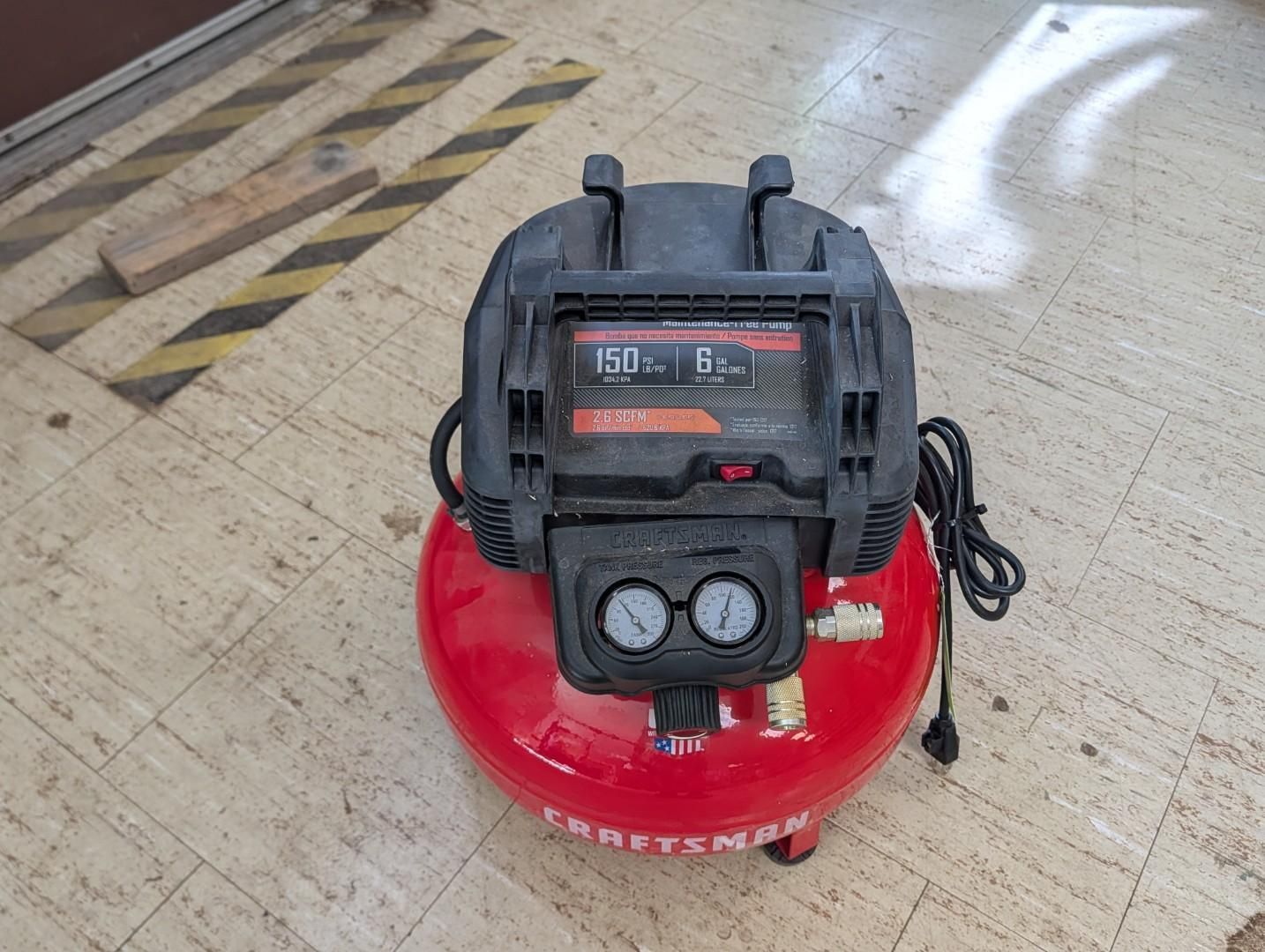 Red air compressor on a tiled floor with a black motor and coiled power cord