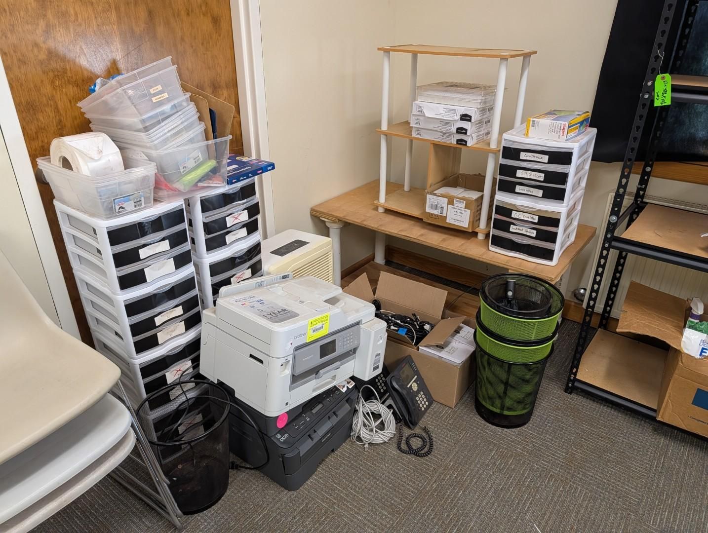 Storage area with stacked plastic bins, boxes, and a small table on a carpeted floor.