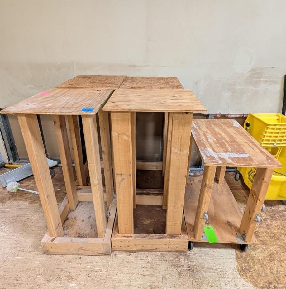 Three unfinished wooden workbenches on a concrete floor against a plain wall.