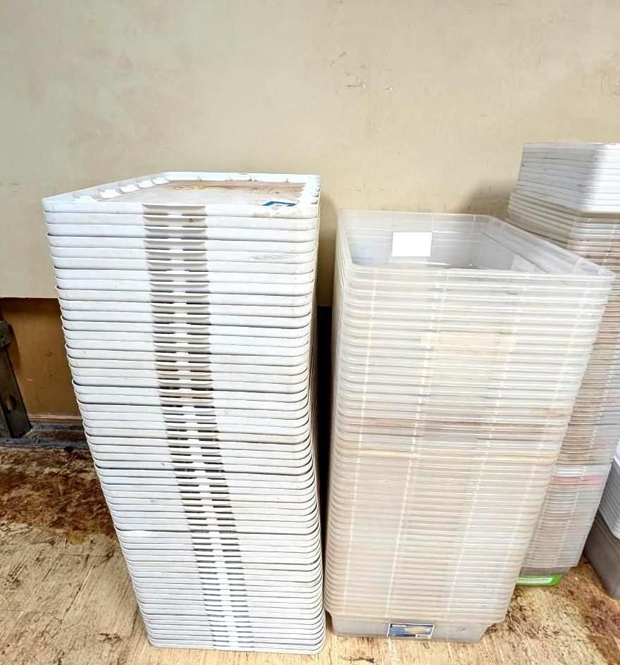 Stacked white plastic trays beside translucent storage bins against a plain wall.