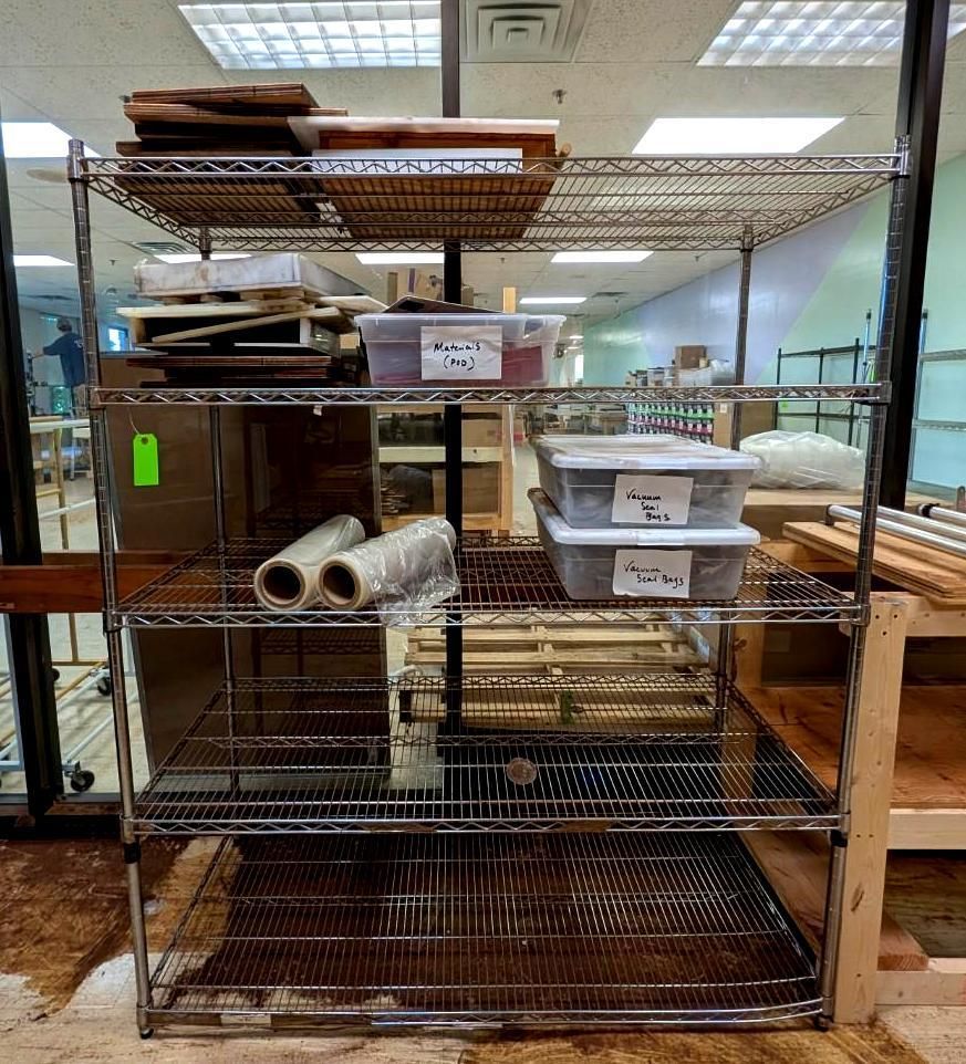 Wire shelving filled with trays, bins, and rolled materials in a workroom or storage area.