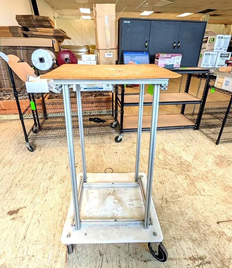 Rolling metal utility cart with a wooden top in a workshop or classroom.
