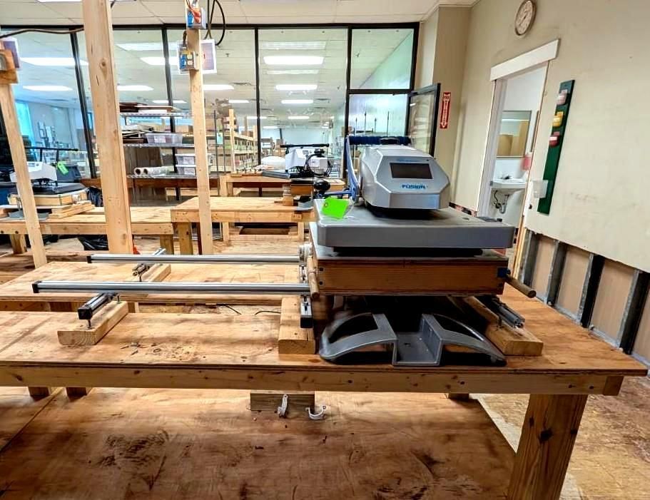 Wooden worktables in a workshop with a gray machine and glass-walled rooms in the background