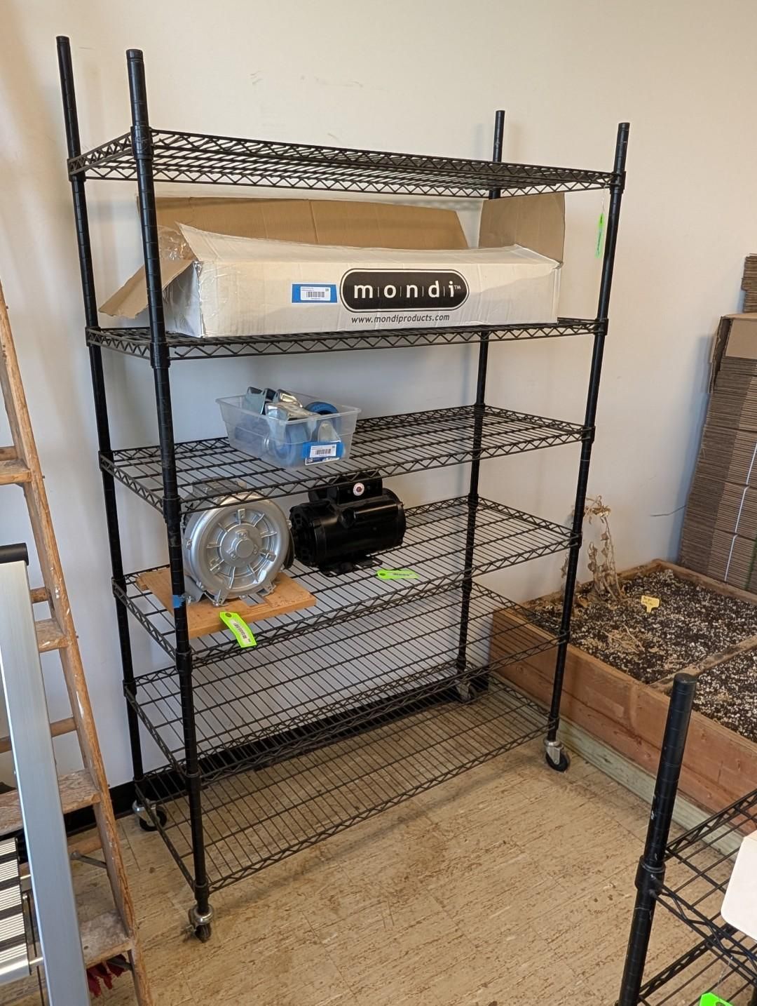 Black metal shelving unit with boxes, bottles, and supplies in a room with a tan carpet.