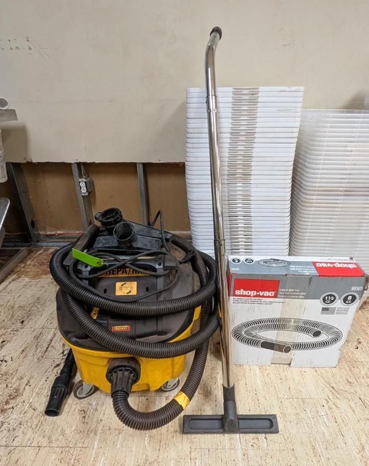 Yellow shop vacuum, coiled hoses, upright floor nozzle, and boxed vacuum attachments on a floor.
