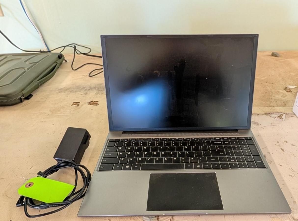 Laptop on a desk with a black power adapter and green-cased cable beside it