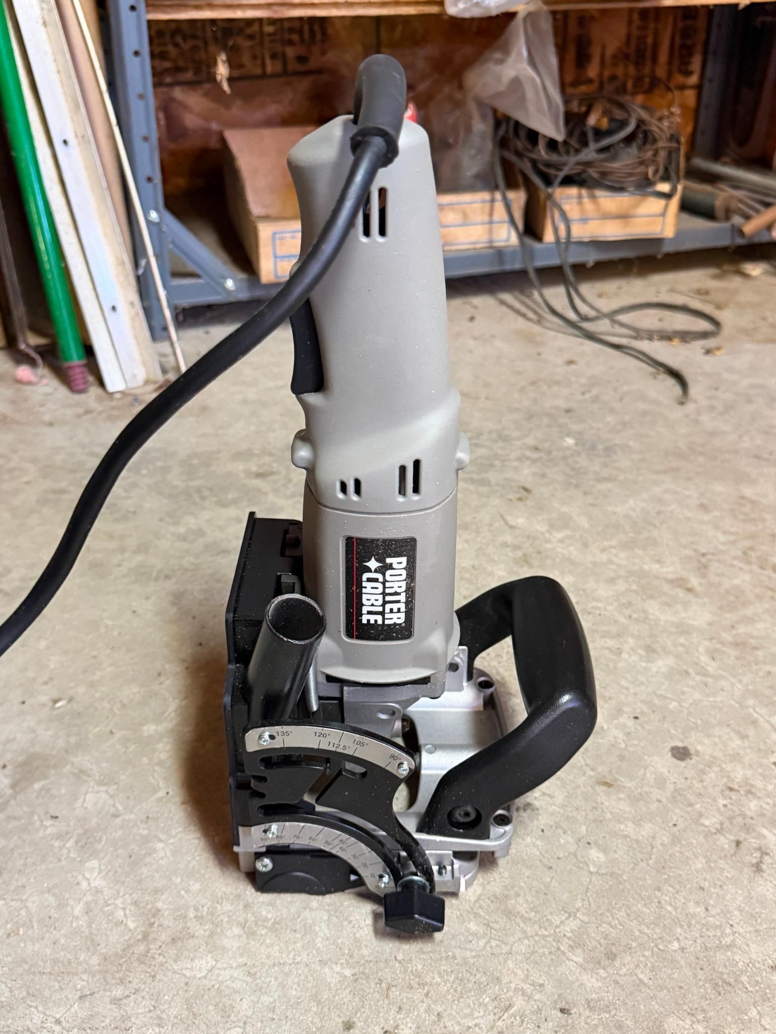 Gray power tool with a black cord standing on a workshop floor