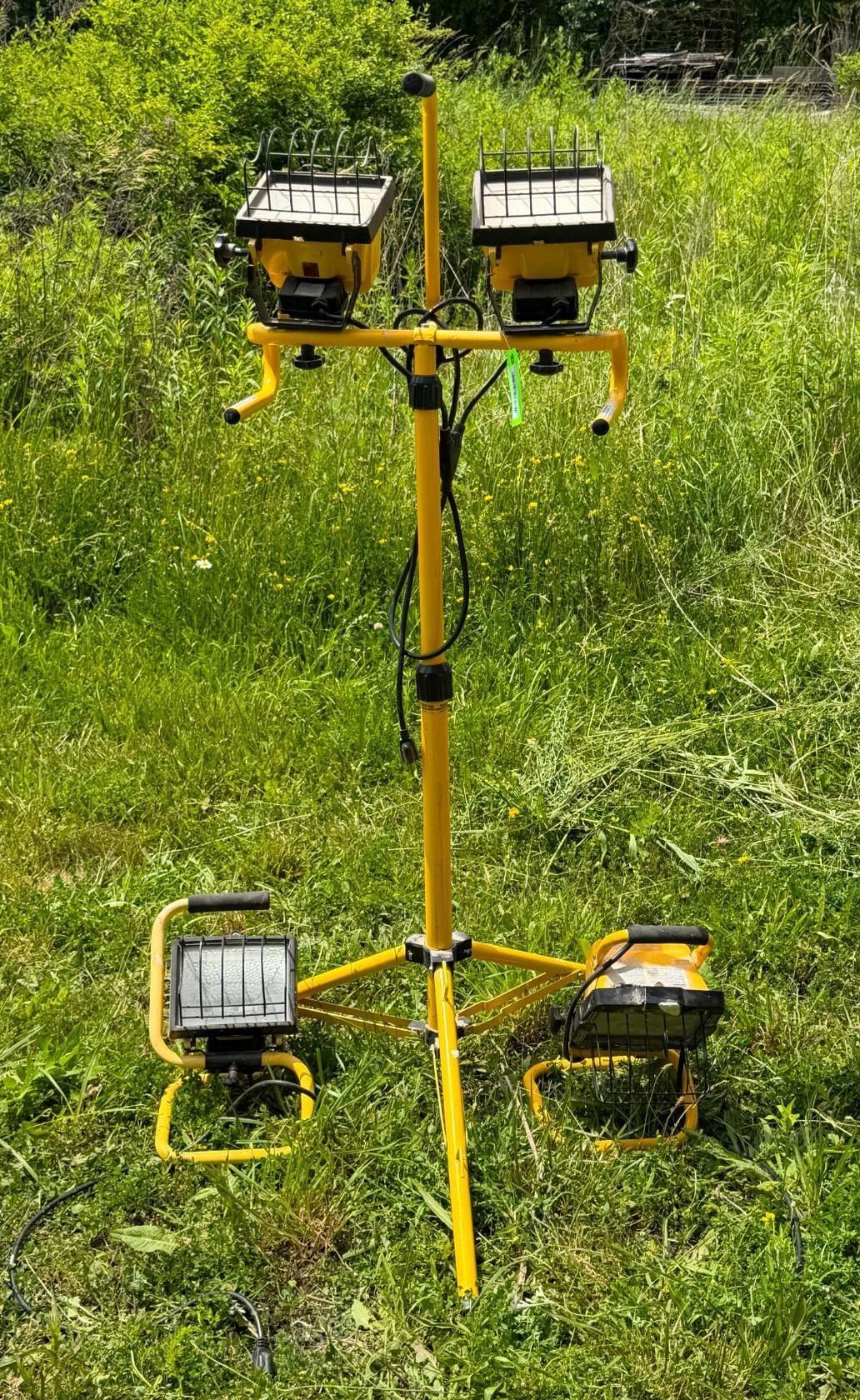 Yellow tripod stand with four mounted floodlights in a grassy field