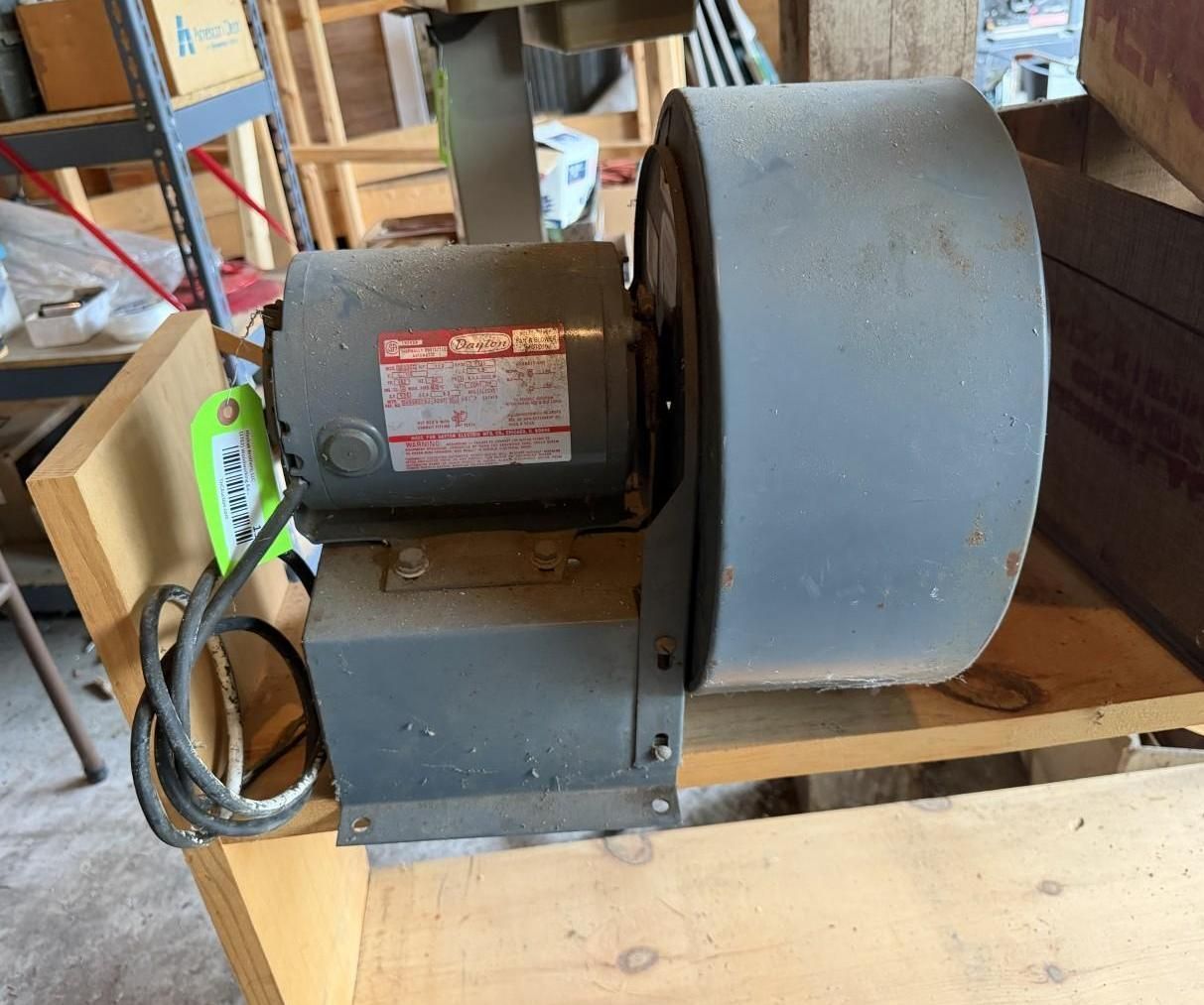 Gray electric blower motor with a large round fan housing on a wooden workbench in a workshop.